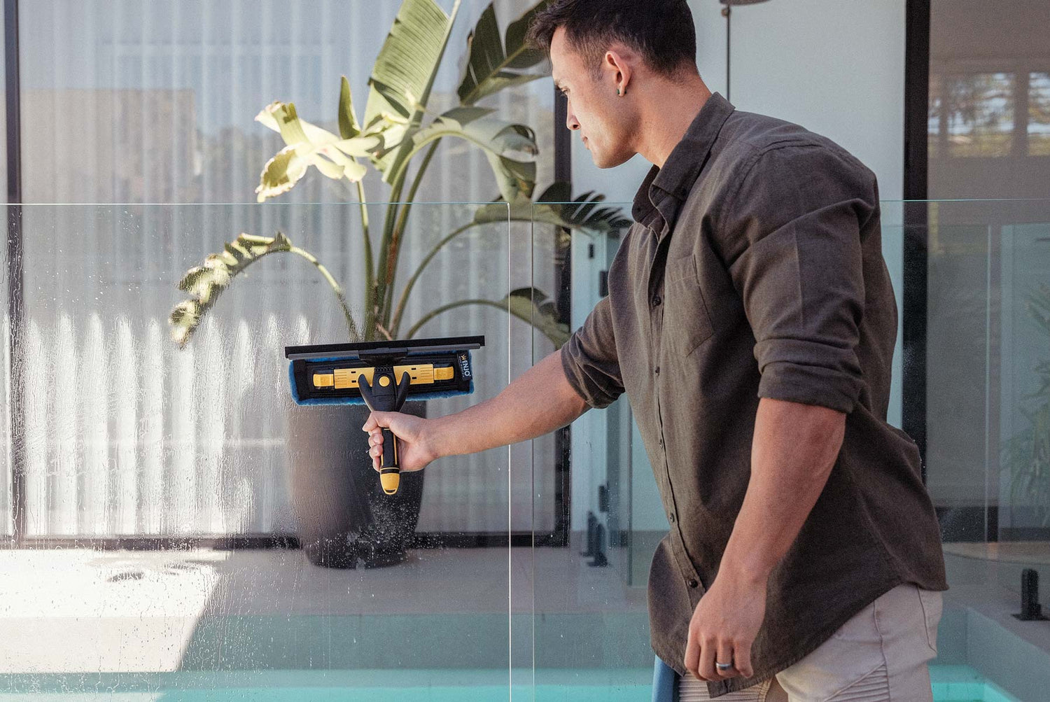 Person cleaning pool glass door with ENJO Window Multi Tool outside