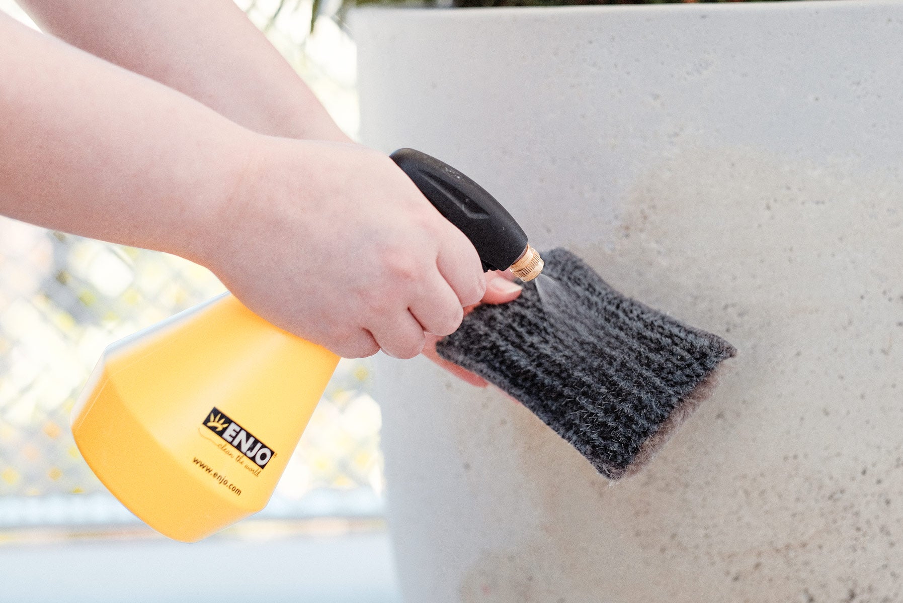 Person wetting ENJO Outdoor Sponge with water using ENJO Trigger Spray Bottle